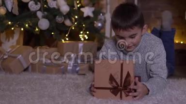 一个小男孩打开一个带礼物的盒子，<strong>高</strong>兴地躺在圣诞树附近的地板上。 <strong>高清高清</strong>